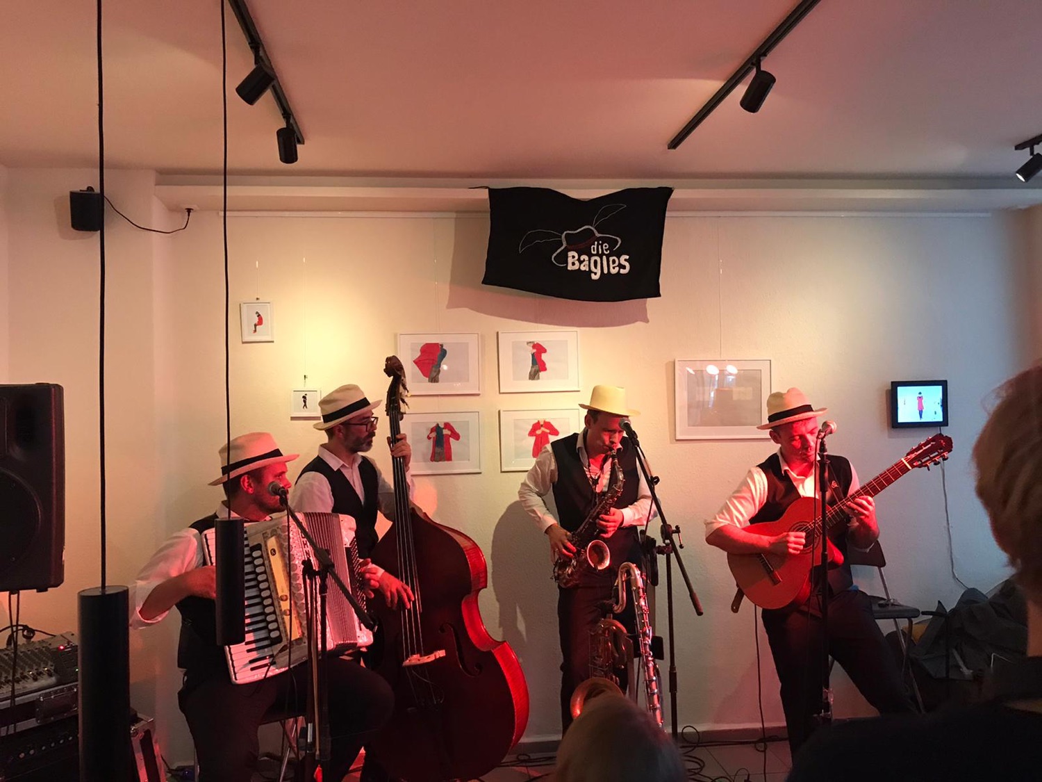 Vier Musiker in weißen Hemden und Hüten spielen in einem Innenraum Akkordeon, Kontrabass, Saxophon und Gitarre