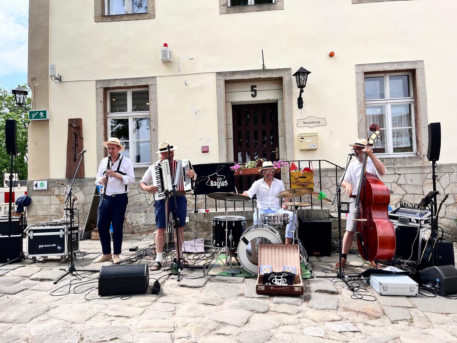Vier Musiker der Die Bagles spielen auf einem gepflasterten Platz Klarinette, Akkordeon, Schlagzeug und Kontrabass